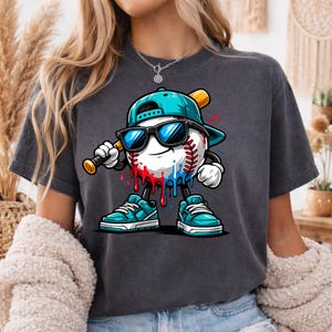 May include: Dark grey t-shirt featuring a baseball character wearing sunglasses and a baseball cap, holding a bat. The baseball has red and blue paint drips. The character is wearing teal sneakers.
