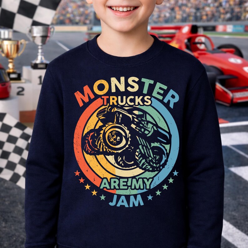 May include: Navy blue sweatshirt with a colorful graphic of a monster truck inside a circle. The text "MONSTER TRUCKS ARE MY JAM" is displayed in a rainbow of colors. The design includes stars and a vintage style.