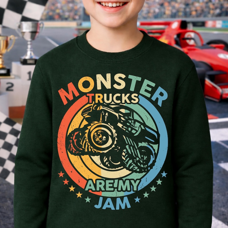 May include: Dark green sweatshirt with a colorful graphic that reads "Monster Trucks Are My Jam." The design features a monster truck inside a circular design with orange, yellow, blue, and green colors. The sweatshirt is worn by a person.