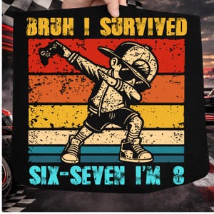Op de afbeelding: Zwart T-shirt met een afbeelding van een kind dat een dab doet, een gamecontroller vasthoudt en een pet draagt. De tekst "BRUH I SURVIVED SIX-SEVEN I'M 8" is gedrukt in geel en turquoise.