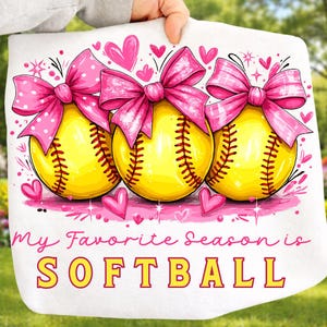 May include: White softball-themed towel with three yellow softballs, each adorned with a pink bow. The text "My Favorite Season is SOFTBALL" is displayed in pink and yellow.