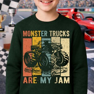 Puede incluir: Sudadera verde oscuro con un gr&aacute;fico de un monster truck y el texto "MONSTER TRUCKS ARE MY JAM" en blanco. El gr&aacute;fico tiene un aspecto vintage y desgastado con rayas naranjas, amarillas, azules y beige. La sudadera la lleva una persona.