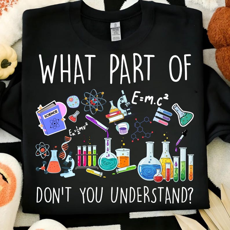 Może przedstawiać: Czarna bluza z okrągłym dekoltem z białym napisem "WHAT PART OF DON'T YOU UNDERSTAND?". Projekt zawiera ilustracje naukowe, takie jak zlewki, prob&oacute;wki i modele atomowe.