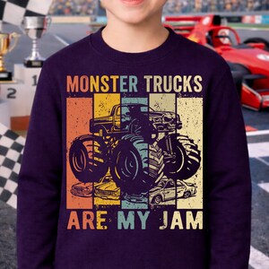Puede incluir: Sudadera morada oscura con un gr&aacute;fico de monster truck y el texto "MONSTER TRUCKS ARE MY JAM". El dise&ntilde;o tiene un aspecto vintage y desgastado, con un fondo de bloques de color en naranja, amarillo, azul y verde.