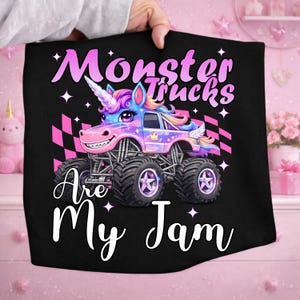 Puede incluir: Camiseta negra con un dise&ntilde;o de cami&oacute;n monstruo unicornio. El cami&oacute;n es una vibrante mezcla de rosa, morado y azul, con neum&aacute;ticos grandes y un emblema en forma de estrella. El texto dice "Monster Trucks Are My Jam."