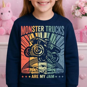 May include: Navy blue sweatshirt with a colorful graphic that says "MONSTER TRUCKS ARE MY JAM." The design features a monster truck, tire tracks, and several cars in a retro style.