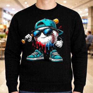 May include: Black sweatshirt featuring a cartoon baseball character wearing sunglasses and a baseball cap. The baseball has red and blue paint drips, and is holding a baseball bat. The character is wearing blue sneakers.