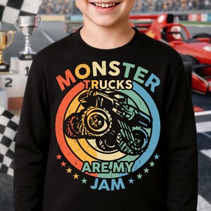 May include: Black sweatshirt with a colorful graphic of a monster truck inside a circle with the text "MONSTER TRUCKS ARE MY JAM". The design features orange, yellow, blue, and green colors, with star accents.