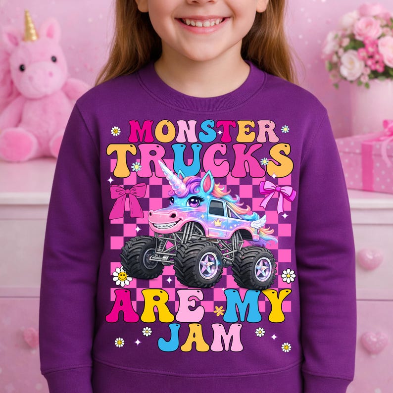 May include: A purple sweatshirt featuring a colorful graphic of a monster truck designed as a unicorn. The text "MONSTER TRUCKS ARE MY JAM" is displayed above and below the truck. The background is a pink and black checkered pattern.