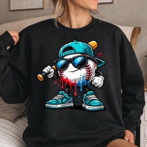 May include: Black sweatshirt featuring a baseball character with sunglasses, a baseball bat, and a teal cap and shoes. The baseball has red and blue paint drips. The design is a cartoon style.