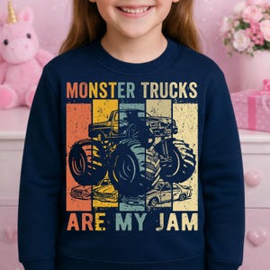 Puede incluir: Sudadera azul marino con un dise&ntilde;o de monster truck. El dise&ntilde;o incluye una imagen de monster truck y el texto "MONSTER TRUCKS ARE MY JAM" en un estilo retro, con un fondo de bloques de color.