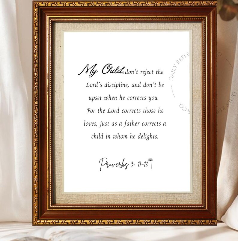 May include: A framed print with a gold-colored ornate frame. The print features the text "My Child, don't reject the Lord's discipline..." and the reference "Proverbs 3: 11-12". The background is a neutral color.