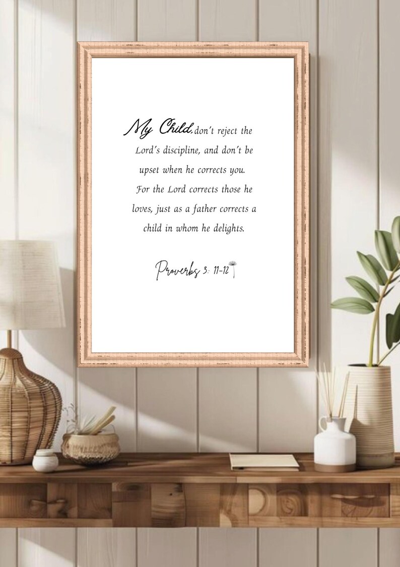 May include: A framed print with a light brown wooden frame. The print features elegant script that reads "My Child... Proverbs 3: 11-12". The text is centered on a white background. The frame is displayed on a wooden shelf.