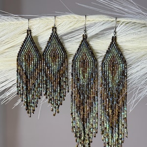 May include: Two pairs of long, teardrop-shaped beaded earrings featuring a woven pattern of metallic brown, bronze, and muted teal glass beads. Each earring has a fringe of dangling beads at the bottom and is attached to a silver-toned metal hook.