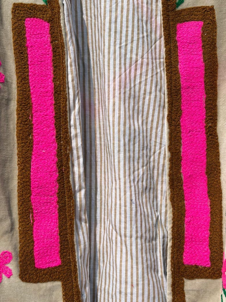 Puede incluir: Primer plano de un textil con fondo beige. El textil presenta un borde marr&oacute;n con un dise&ntilde;o rectangular rosa brillante. El interior del textil tiene un patr&oacute;n de rayas en beige y blanco.