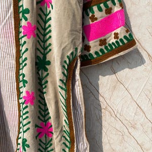 Puede incluir: Chaqueta de terciopelo beige con bordados florales. La chaqueta presenta flores rosas brillantes y hojas verdes bordadas en la parte delantera y las mangas. Las mangas tienen un ribete marr&oacute;n y una franja rosa. La chaqueta tiene un forro a rayas.