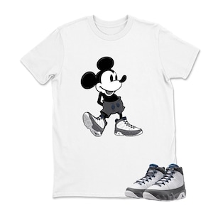 May include: White t-shirt featuring a black and white cartoon Mickey Mouse graphic. The image also shows a pair of white and gray sneakers with blue accents, creating a coordinated look.