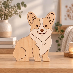 Könnte beinhalten: Ein helles Holzpuzzle in Form eines Corgi-Hundes. Die Figur besteht aus zwei verschiedenen Holztönen, wobei ein dunklerer Ton für die Ohren und den oberen Kopfbereich und ein hellerer Ton für Brust und Körper verwendet wurde, mit sichtbaren Puzzleteilen.