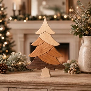 May include: A decorative wooden Christmas tree sculpture composed of four stacked, interlocking segments. Each segment features a distinct wood grain and color, ranging from light beige at the top and base to medium and dark brown in the middle.