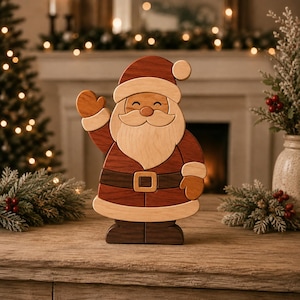 Op de afbeelding: Een decoratief houten kerstmanfiguur met een gelaagd ontwerp in lichte en donkere houttinten. Het figuur stelt de kerstman voor die zwaait met een glimlachend gezicht, een witte baard, een rode muts, een donkere riem met gesp en bruine laarzen.