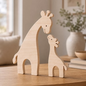 Puede incluir: Dos figuras de jirafa de madera de color claro, una más grande y otra más pequeña, de pie una al lado de la otra. Las figuras presentan superficies lisas y planas con contornos tallados simples que representan las cabezas, cuellos, cuerpos y colas.