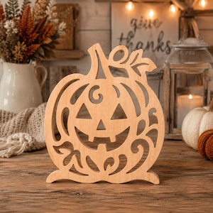 Può includere: Una sagoma in legno di colore chiaro a forma di zucca di Halloween con intricati dettagli a volute e foglie. La zucca presenta un classico volto intagliato con occhi triangolari e un ampio sorriso, poggiata su una base piatta.