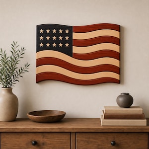 May include: A wall-mounted wooden American flag featuring a wavy design with a dark blue canton containing twelve light-colored stars. The flag consists of alternating horizontal stripes in deep reddish-brown and light tan wood tones.