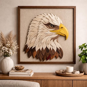 Puede incluir: Una obra de arte mural de madera que representa una detallada cabeza de águila calva. Las plumas del águila están hechas de varias tonalidades de madera, con un pico amarillo y un ojo marrón. La obra de arte está enmarcada en un marco de madera marrón oscuro.