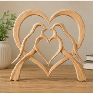 May include: A light-colored wooden sculpture featuring two birds facing each other, their bodies and beaks forming a large heart shape outline with a smaller heart shape cutout in the center. The piece has a smooth, natural wood grain finish.