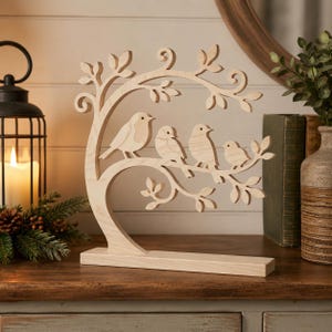 Può includere: Una scultura in legno chiaro intagliato che raffigura un albero stilizzato con rami curvi e foglie. Quattro uccelli di varie dimensioni sono appollaiati sui rami. L'intero pezzo è montato su una base rettangolare in legno per stabilità.