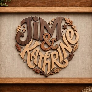 Puede incluir: Obra de arte enmarcada en madera con los nombres "Jim & Kathrine" en forma de corazón. Los nombres están hechos de madera en tonos marrones y beige, con detalles de hojas y estrellas. La obra se presenta sobre un fondo de lino neutro.