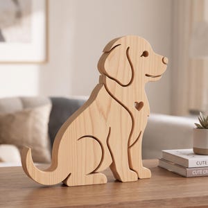 May include: A light-coloured wooden dog figurine featuring a smooth, natural grain finish. The design depicts a seated dog in profile with a small heart-shaped cutout on the chest area, clean lines, and a minimalist silhouette structure.