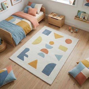 May include: A child's bedroom with a wooden bed, bedding, and pillows in shades of blue, orange, and yellow. A white rug with colorful geometric shapes is on the floor. Wooden toy chest and framed art complete the room.