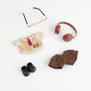 Puede incluir: Colecci&oacute;n de ropa y accesorios de mu&ntilde;ecas en miniatura, que incluye un chaleco de punto beige con corbata roja, pantalones cortos marrones, zapatos negros, gafas y auriculares marrones. El chaleco tiene un parche "HAPPY".