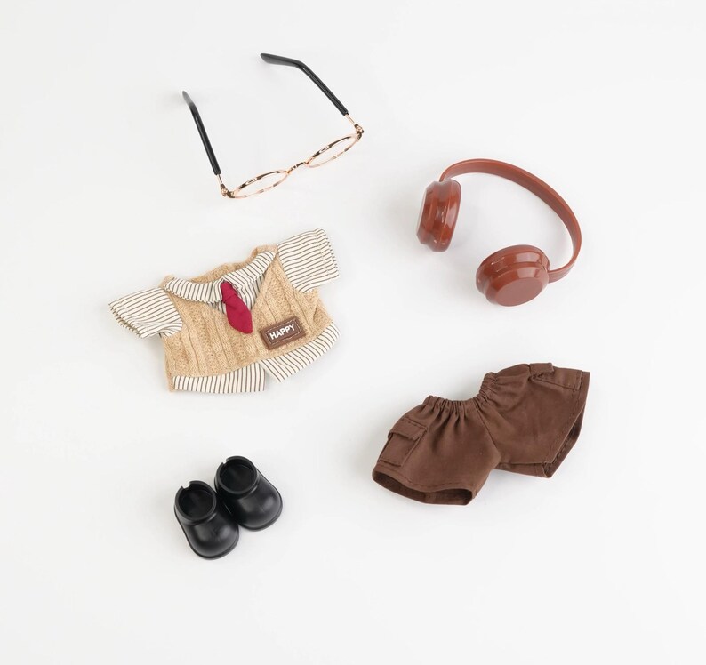 Puede incluir: Colecci&oacute;n de ropa y accesorios de mu&ntilde;ecas en miniatura, que incluye un chaleco de punto beige con corbata roja, pantalones cortos marrones, zapatos negros, gafas y auriculares marrones. El chaleco tiene un parche "HAPPY".
