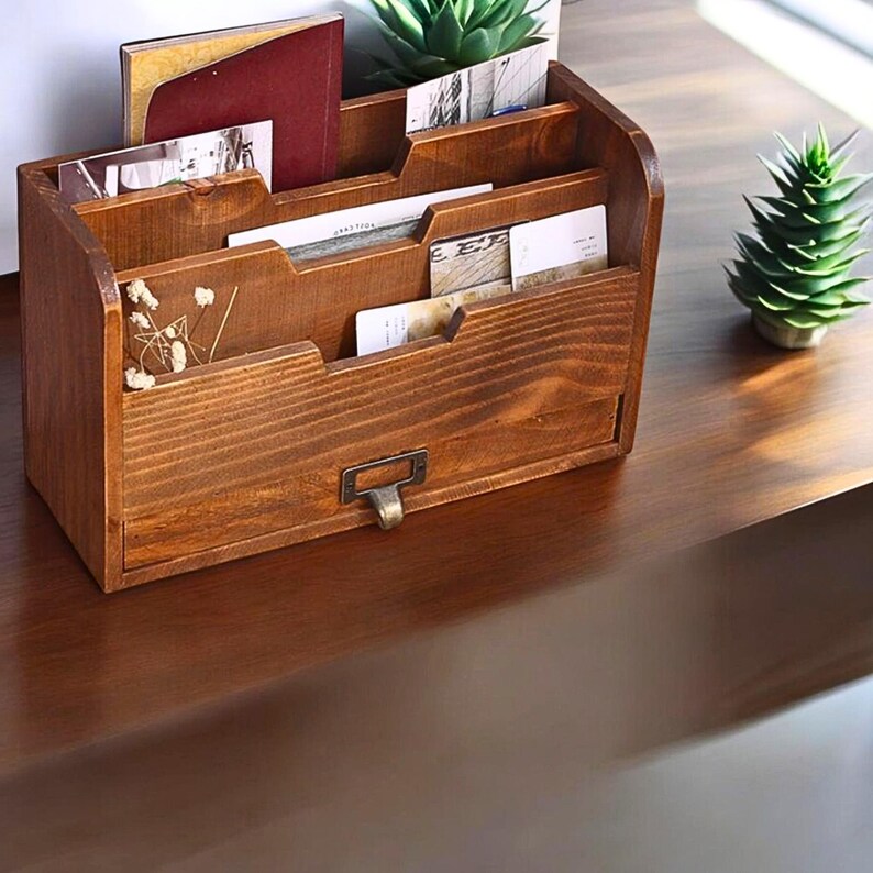 May include: A wooden desk organizer with multiple compartments and a small drawer. The organizer is stained a warm brown color and holds various cards and small notebooks. A small brass-colored pull is on the drawer.