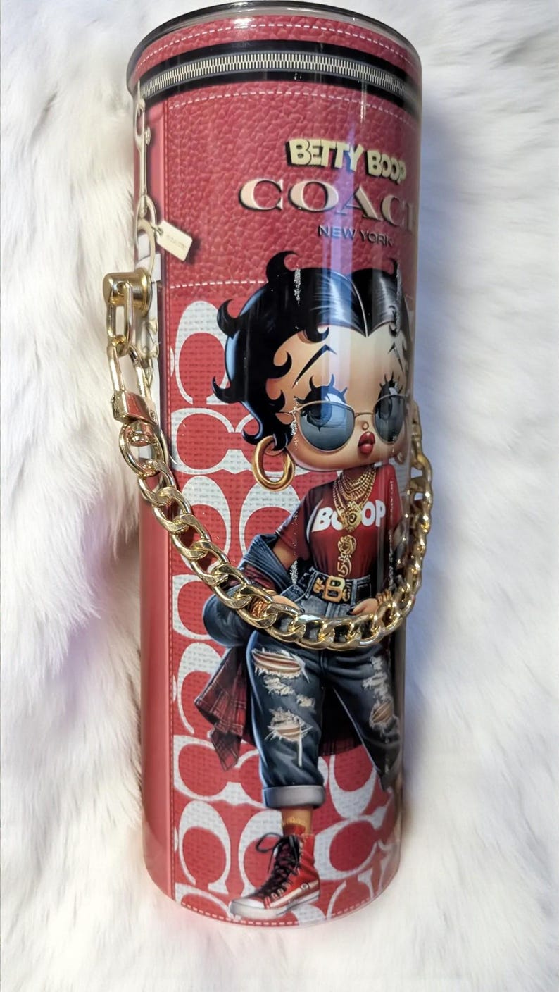 May include: A red and white tumbler featuring a Betty Boop illustration in a stylish outfit, with the text "BETTY BOOP COACH NEW YORK". The tumbler has a gold chain handle and a zipper design.
