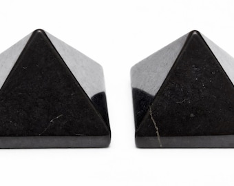 May include: Two black pyramid-shaped objects with a glossy finish are shown against a white backdrop. The pyramids have a geometric design and are likely decorative or collectible items.