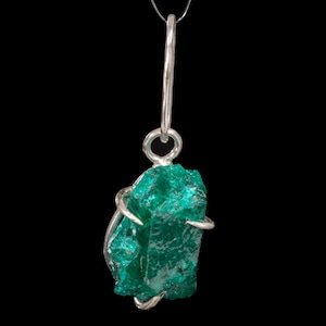 May include: A vibrant green gemstone pendant with a silver wire wrap and a silver loop for hanging. The rough-cut stone has a natural, textured appearance, suspended from a thin, clear cord against a black background.