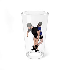 May include: A clear glass pint glass with a cartoon illustration of two people wearing helmets. One person is carrying the other on their back. The person being carried is wearing a blue shirt and black shorts. The other person is wearing a black shirt and shorts.