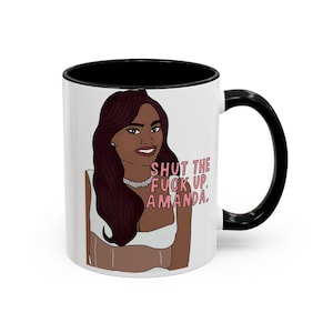 May include: White ceramic mug with a black interior and handle. The mug features a cartoon illustration of a woman with the text "SHUT THE FUCK UP, AMANDA." printed in pink.