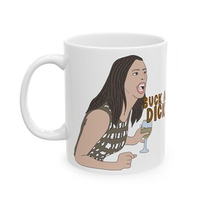 May include: White ceramic mug featuring a cartoon illustration of a woman yelling, holding a wine glass. The mug has the text "SUCK A DICK" in brown letters. The woman is wearing a patterned top and has brown hair.