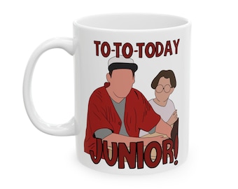 May include: White ceramic mug with a cartoon illustration and the text "TO-TO-TODAY JUNIOR!". The design features two figures, one in a red jacket and the other in a white shirt. The mug has a curved handle.