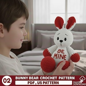 May include: A white and red crochet bunny bear with the text "BE MINE" on its chest. The bunny bear has red ears, paws, and a red ball. The image also includes the text "BUNNY BEAR CROCHET PATTERN PDF, US PATTERN".