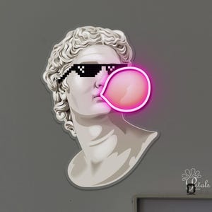Peut inclure: Un buste blanc d'une figure classique portant des lunettes de soleil pixélisées et soufflant une bulle de chewing-gum rose. Le buste est monté sur un mur gris. Une carte en noir et blanc et un tourne-disque sont visibles en arrière-plan.