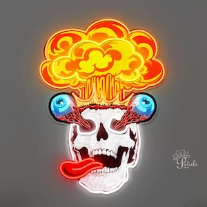 May include: A neon sign featuring a skull with a red tongue, bulging eyes, and a mushroom cloud explosion. The sign is white, red, orange, and yellow. The sign is mounted on a gray wall above a wooden shelf.