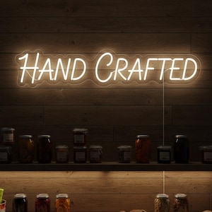 Puede incluir: Un letrero de neón que dice "HAND CRAFTED" en una pared de madera. Debajo, estantes con frascos de conservas, pan, queso y otros alimentos, lo que sugiere productos alimenticios artesanales.