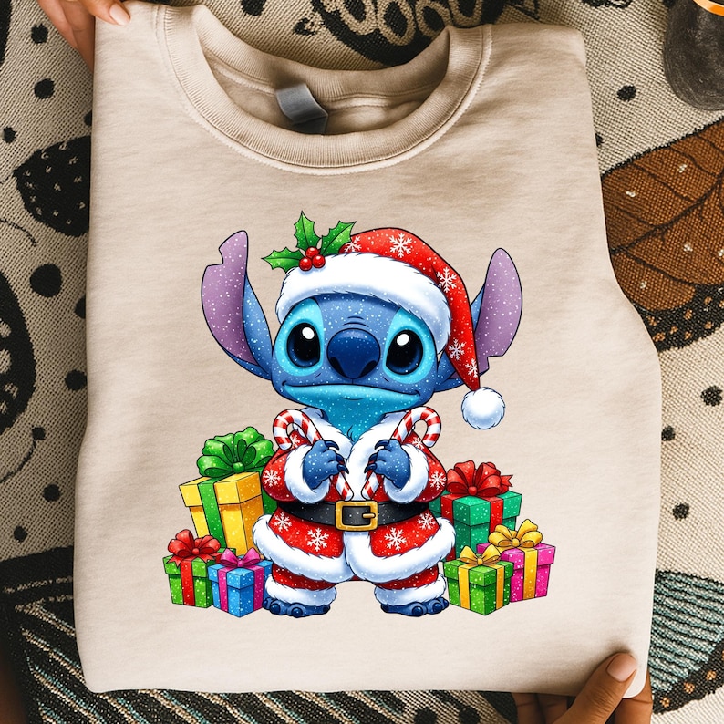 Puede incluir: Sudadera beige con un personaje de dibujos animados, Stitch, vestido con un traje de Pap&aacute; Noel. El personaje azul lleva un gorro y abrigo de Pap&aacute; Noel rojo y blanco, sosteniendo bastones de caramelo. Regalos coloridos rodean al personaje, tema navide&ntilde;o.