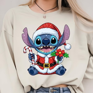 Puede incluir: Sudadera beige con un personaje de dibujos animados navide&ntilde;o. El personaje, un extraterrestre azul, viste un traje y gorro de Pap&aacute; Noel, sosteniendo un bast&oacute;n de caramelo y una flor. El dise&ntilde;o es colorido y detallado, ideal para la temporada.