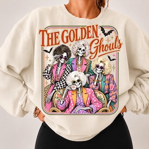 May include: A cream-colored crewneck sweatshirt featuring a graphic print of four skeletons with blonde, curly hair wearing colorful blazers and sunglasses. The text reads The Golden Ghouls, accompanied by illustrations of small black bats and stars.